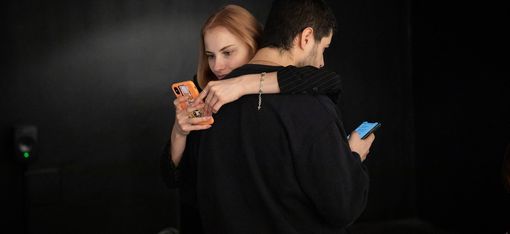 Zwei Personen stehen Rücken an Rücken, beide halten ein Smartphone in der Hand.