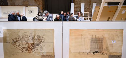 In the foreground are two very large pictures on the floor. Behind them, you can only see the heads of about 10 people.