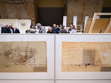 In the foreground are two very large pictures on the floor. Behind them, you can only see the heads of about 10 people.