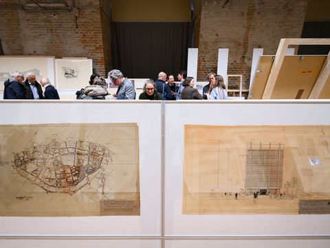 In the foreground are two very large pictures on the floor. Behind them, you can only see the heads of about 10 people.