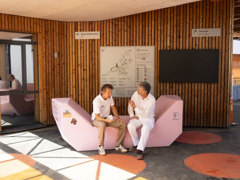 Two people sit on a pink Enzi talking at the Schafberg mountain station.
