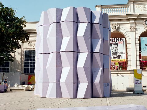 Hoher Turm aus gestapelten lilafarbenen Enzi-Elementen auf dem Platz im MuseumsQuartier, vor der Fassade der Kunsthalle Wien.