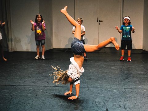 In the centre of the photo, a child is doing a handstand. The other four children are watching and clapping.