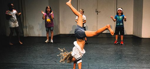 In the centre of the photo, a child is doing a handstand. The other four children are watching and clapping.