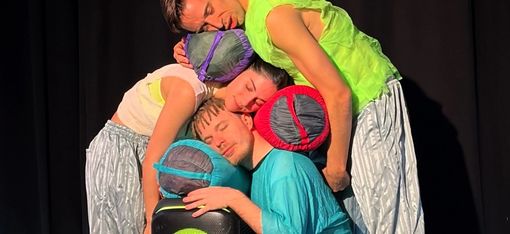 Three dancers have closed their eyes and stacked their heads and sleeping bags on top of each other.