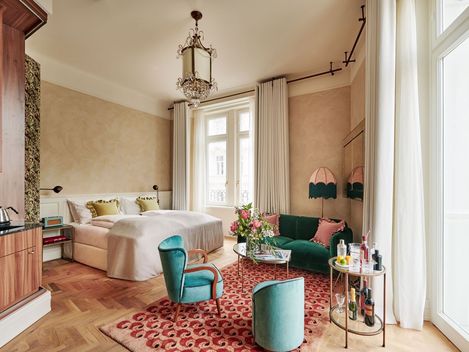 Elegantes Schlafzimmer in Pastelltönen mit einem weichen Bett, einem Vintage-Kronleuchter, einem zartgrünen Sofa und rosa Akzenten. Gemütliche, stilvolle Atmosphäre.
