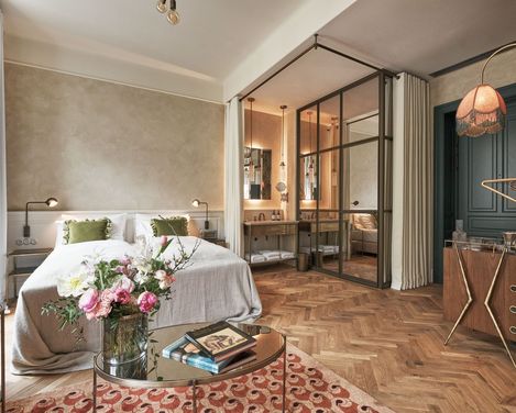 Ein gemütliches Schlafzimmer verfügt über ein weiches Doppelbett mit grünen Kissen und einer grauen Decke. Frische Blumen auf einem Glastisch und eine warme Beleuchtung schaffen eine ruhige Atmosphäre.