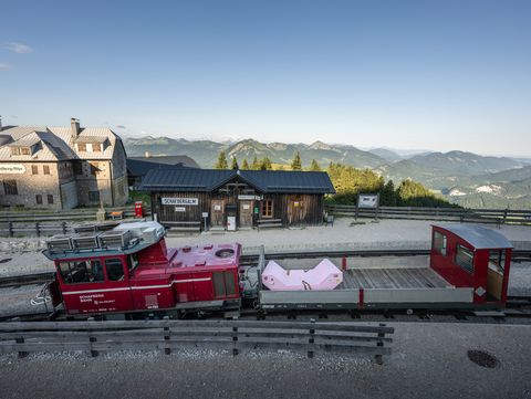 Pink Enzi on a transport wagon at Schafbergalpe station with panoramic Alpine views.