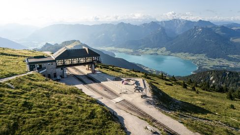 Aerial view of the Schafberg mountain station with a pink Enzi overlooking Lake Wolfgang and the Alps.
