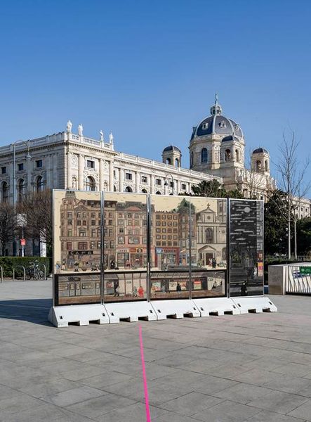 Pillars displaying colored-pencil drawings on both sides stand against an urban backdrop.