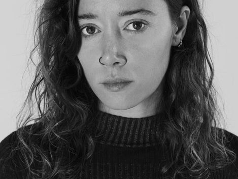 Person with shoulder-length wavy hair and earring wearing a black turtleneck sweater.