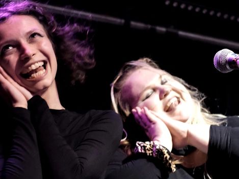 Two young people are standing on stage, singing. They’re clearly having a great time.