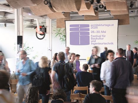 Im Hintergrund befindet sich eine Leinwand mit mit der Ausschrift: architekturtage.at 2026
Im Vordergrund stehen und sitzen ca. 20 Personen und unterhalten sich angeregt.