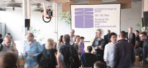 Im Hintergrund befindet sich eine Leinwand mit mit der Ausschrift: architekturtage.at 2026
Im Vordergrund stehen und sitzen ca. 20 Personen und unterhalten sich angeregt.