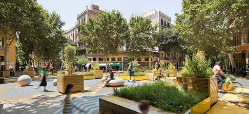 Several people are gathered in a beautiful, newly created square. Patterns on the ground break up the large open space, with several seating areas dotted amongst them. There are large planters containing trees and greenery. A residential building can be seen in the background.