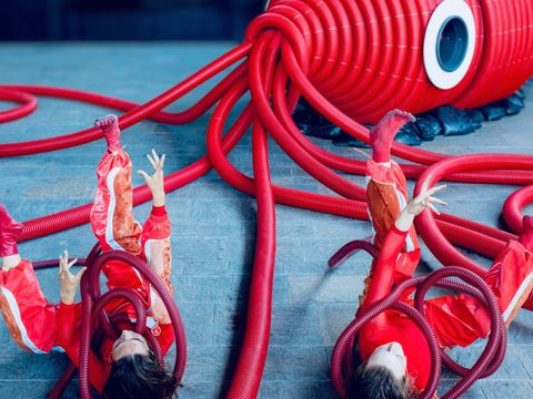 Two female performers are lying on their backs on the floor. They are struggling against the tentacles that are wrapping around them.