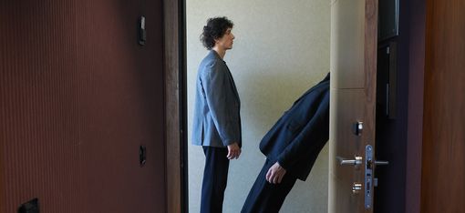 A view through the open door of a hotel room. One performer is standing upright; the other appears to be falling backward.