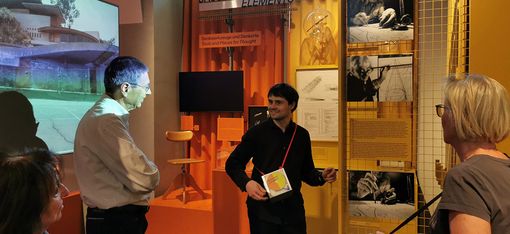 During a guided tour of the Architekturzentrum Wien, a group of people are standing together in the permanent exhibition, listening to the guide.