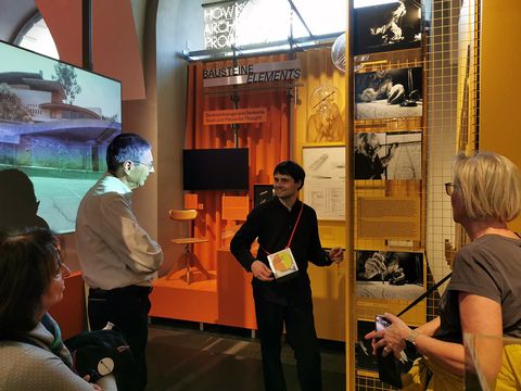 During a guided tour of the Architekturzentrum Wien, a group of people are standing together in the permanent exhibition, listening to the guide.