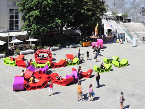 Bunte Enzo-Sitzmöbel im MuseumsQuartier Wien, Menschen sitzen, liegen und bewegen sich zwischen den modularen Möbeln auf dem Platz.