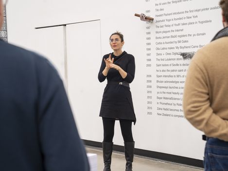 Eine Person steht im Ausstellungsraum vor einem Kunstwerk und verdolmetscht eine Führung in Gebärdensprache.
