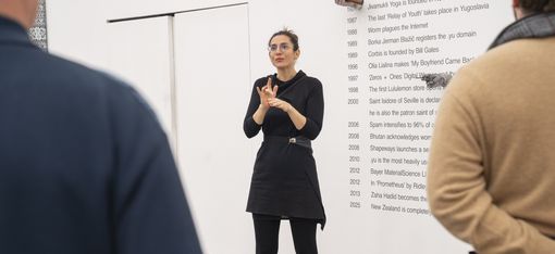 Eine Person steht im Ausstellungsraum vor einem Kunstwerk und verdolmetscht eine Führung in Gebärdensprache.