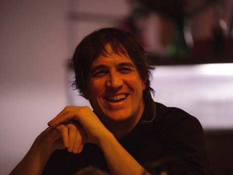 Person with blurred face sitting with clasped hands against a blurred background.