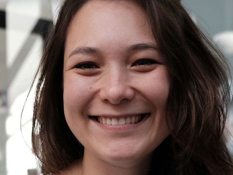 Portrait of a smiling young woman with long dark hair against a blurred background.