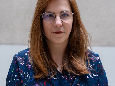 Woman with shoulder-length straight hair wearing a blue top with colorful pattern against gray background.