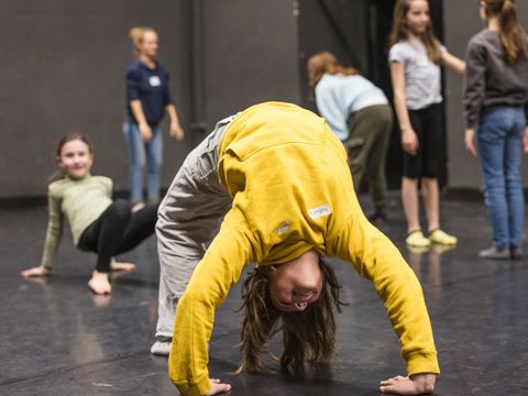 Children are on a dance floor. The child in the foreground is doing a “bridge”.