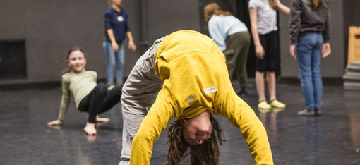 Children are on a dance floor. The child in the foreground is doing a “bridge”.