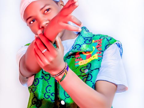 Person wearing a headscarf and green patterned sleeveless vest over a white t-shirt pointing forward with one hand.