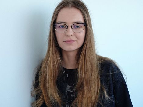 Woman with long brown hair and glasses against a white background