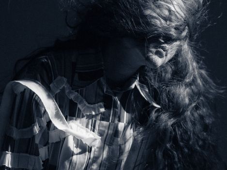 Woman with long, tousled hair wearing a striped shirt against a dark background.