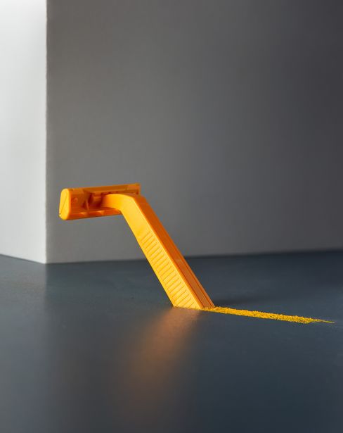 Orange disposable razor angled out of a smooth surface leaving a line of orange powder.