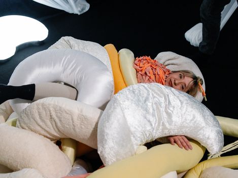 Eine Frau kuschelt sich in weiche Pölster und Stoffe.