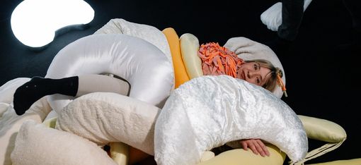 Eine Frau kuschelt sich in weiche Pölster und Stoffe.