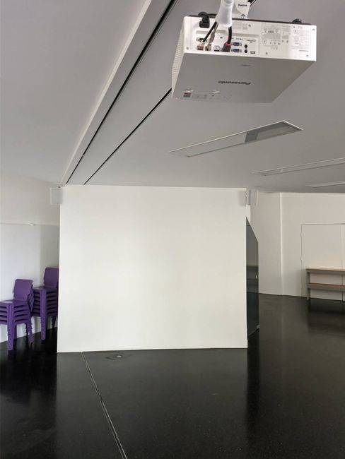 Interior view of Room D: projector and projection screen with a stack of chairs