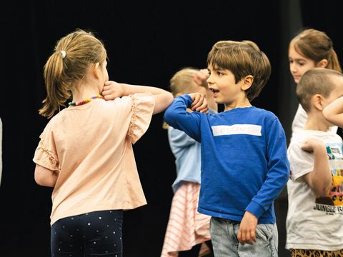 In the centre of the photo are two children standing side by side, smiling at each other.