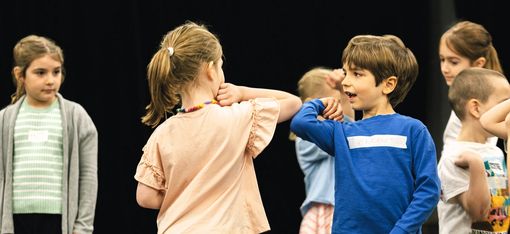 In the centre of the photo are two children standing side by side, smiling at each other.