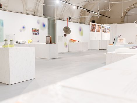 Helle Museums-Ausstellung mit weißen Podesten, Posterwänden, Skulpturen und Lichtinstallationen.