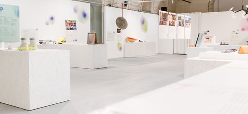Bright, airy gallery with white pedestals, posters and eclectic displays including shoes and a sculptural orb.
