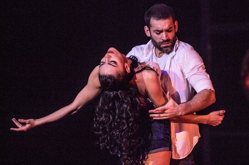 Dance scene with a man in a white shirt with a dramatic expression on his face and a woman with dark curly hair leaning backwards.