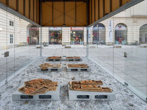 Frontal view of the MQ Art Box featuring an installation of textile objects on platforms with scattered metal fragments inside.