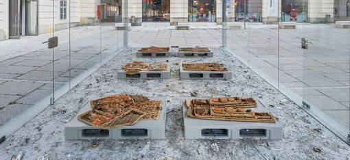 Frontal view of the MQ Art Box featuring an installation of textile objects on platforms with scattered metal fragments inside.