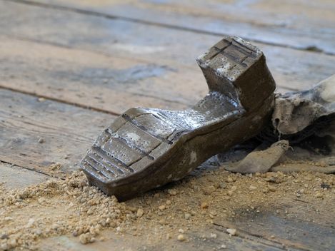 A ceramic shoe lies upside down on a wooden floor, surrounded by gravel.