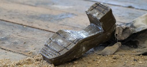 A ceramic shoe lies upside down on a wooden floor, surrounded by gravel.