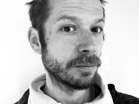 Portrait of a man with short hair and beard wearing a zip-up sweater with a raised collar.