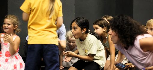The children and the workshop leader are kneeling on the dance floor, their smiling gazes directed to something invisible on the left.