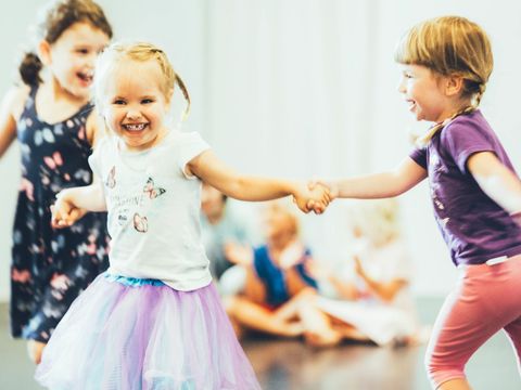 Three girls are holding hands and dancing in a semicircle.